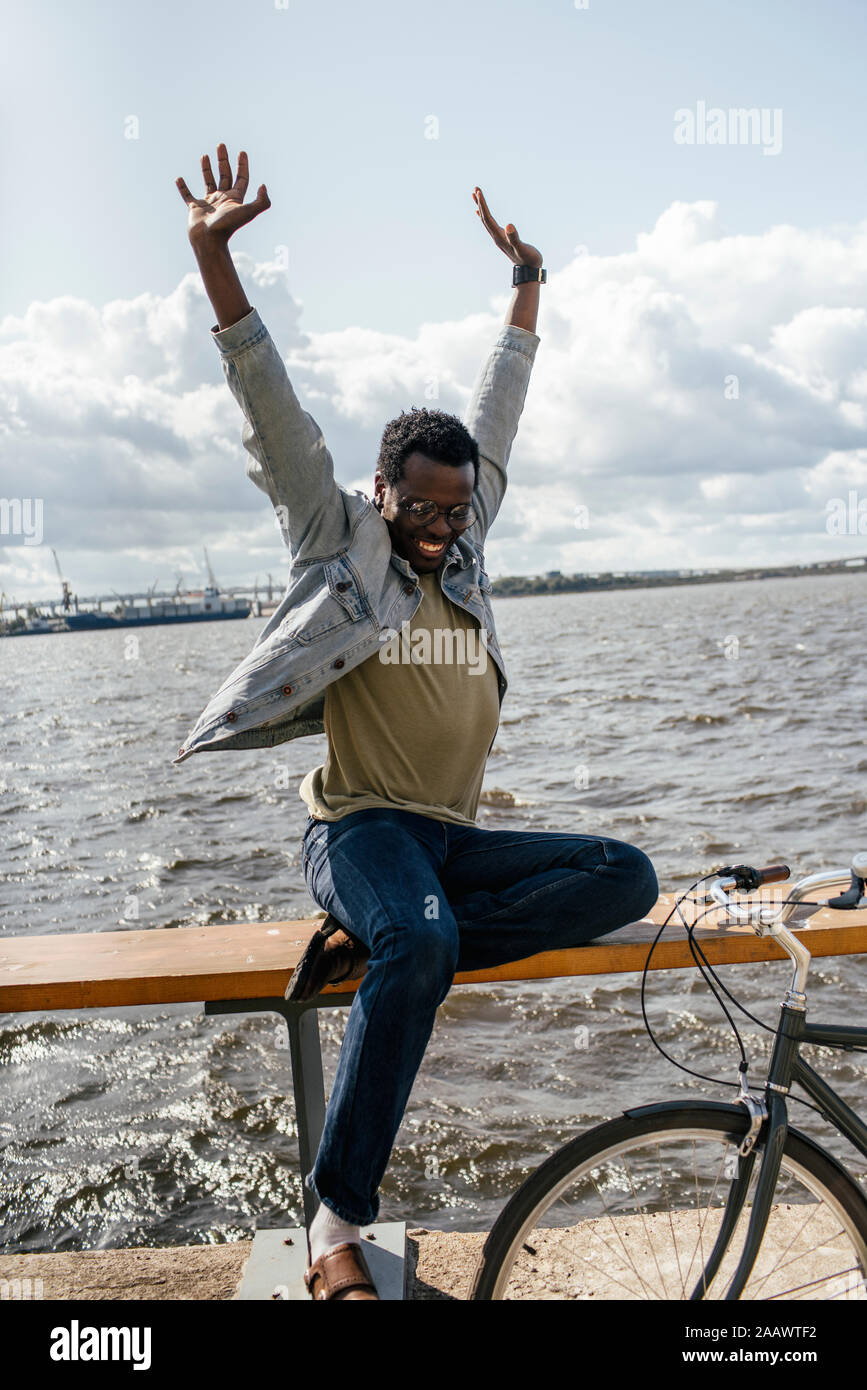 Jeune homme à vélo, assis sur railng par la mer, en faisant semblant de voler Banque D'Images