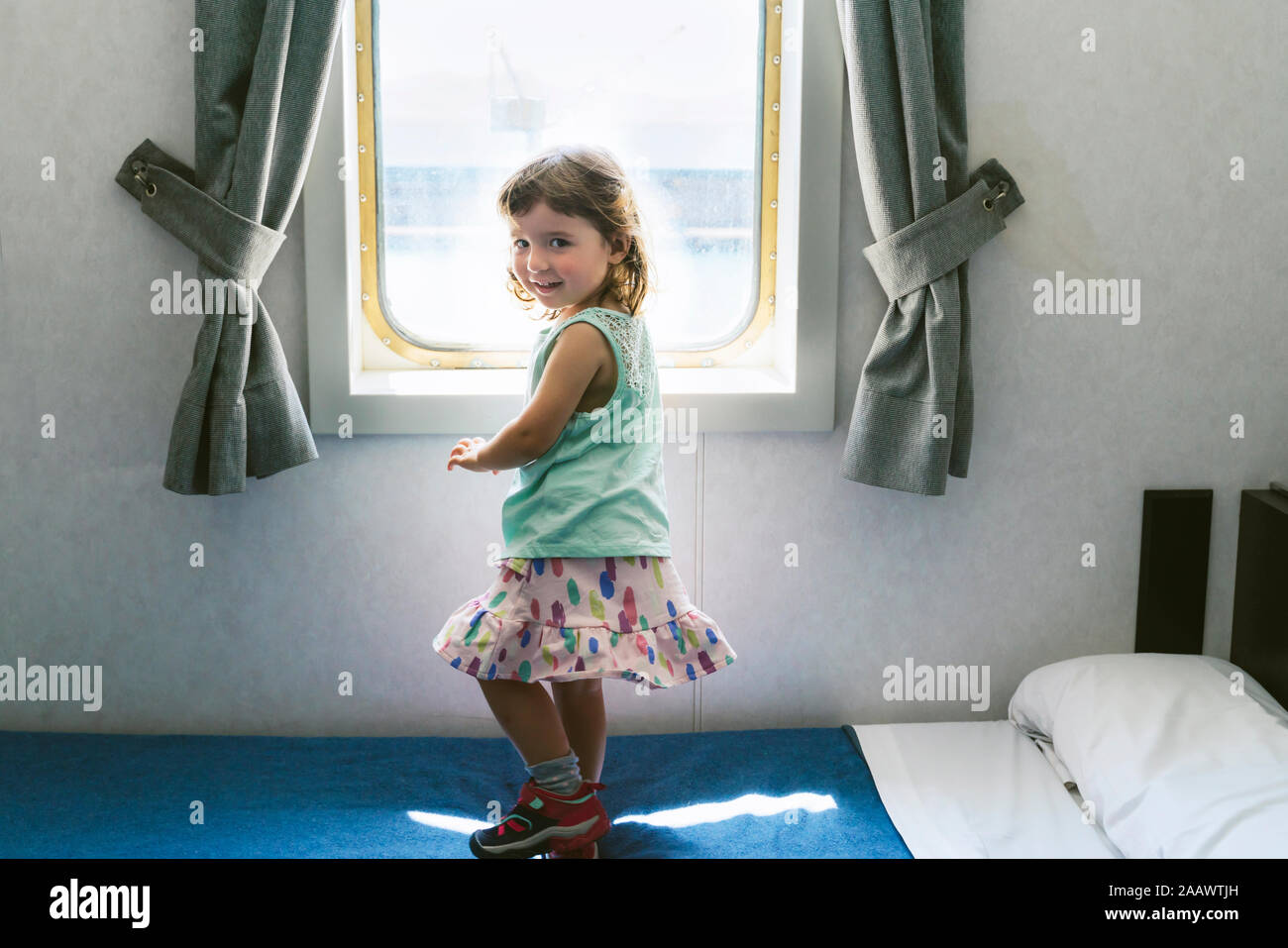 Portrait de petite fille debout sur lit de cabine du navire en face de la fenêtre Banque D'Images