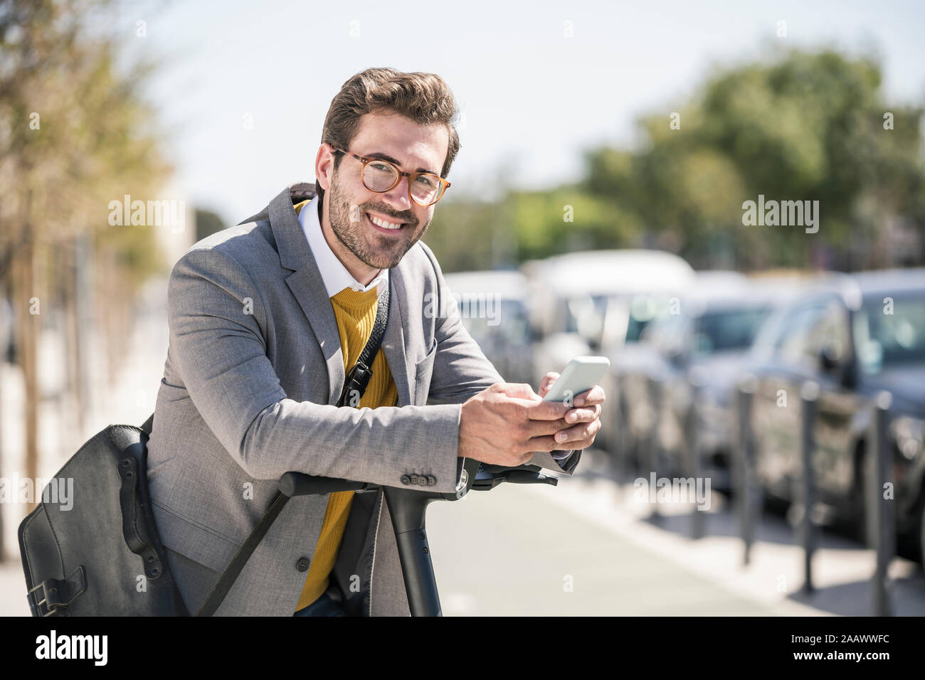 Portrait of smiling young woman with cell phone et l'e-scooter dans la ville Banque D'Images