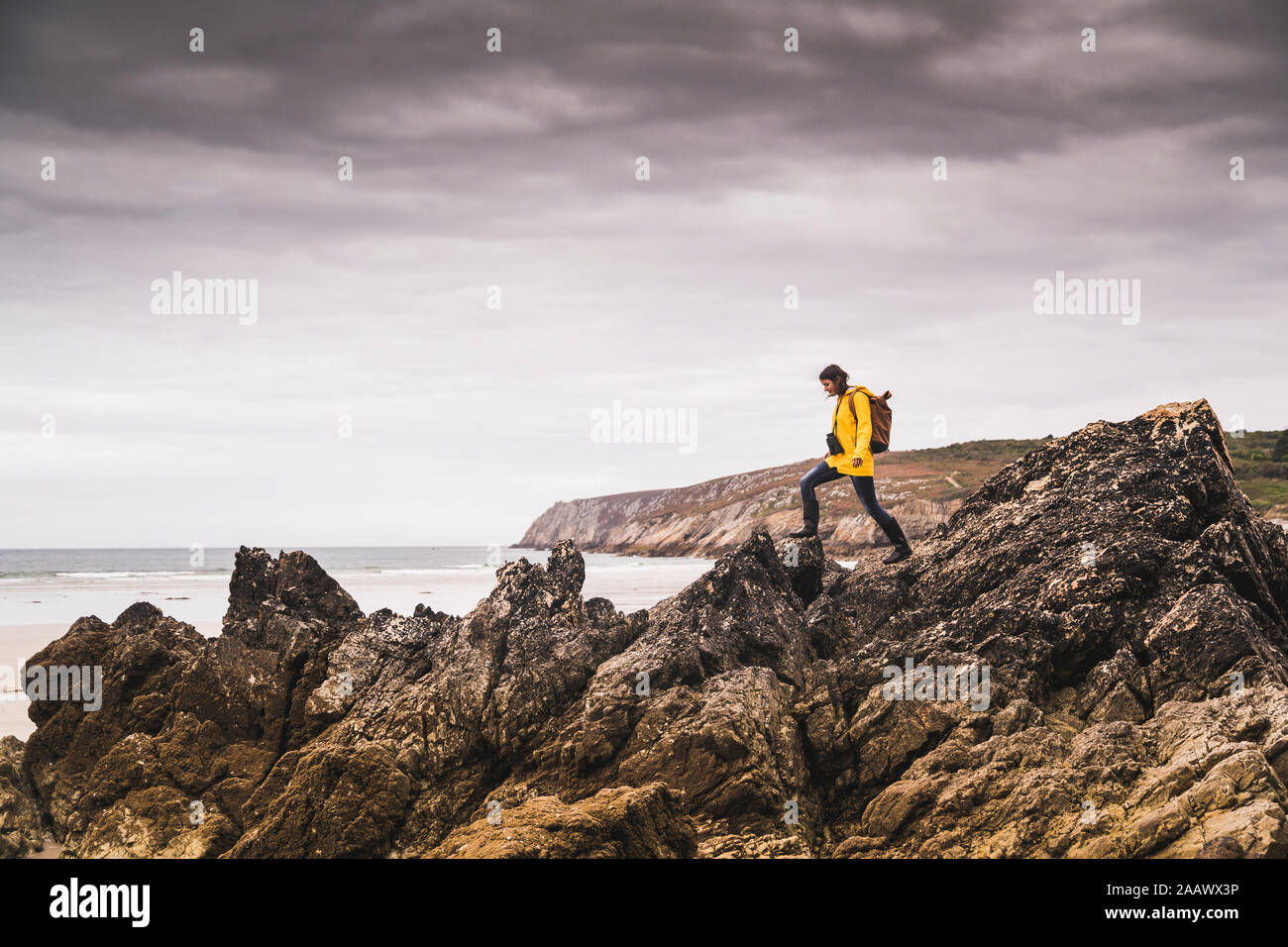 Jeune femme portant Veste pluie jaune sur la plage, regardant à travers des jumelles, Bretagne, France Banque D'Images