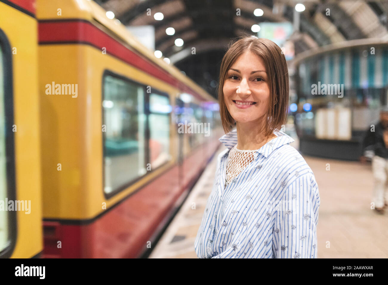 Jeune femme souriante sur gare avec train trouble dans l'arrière-plan Banque D'Images