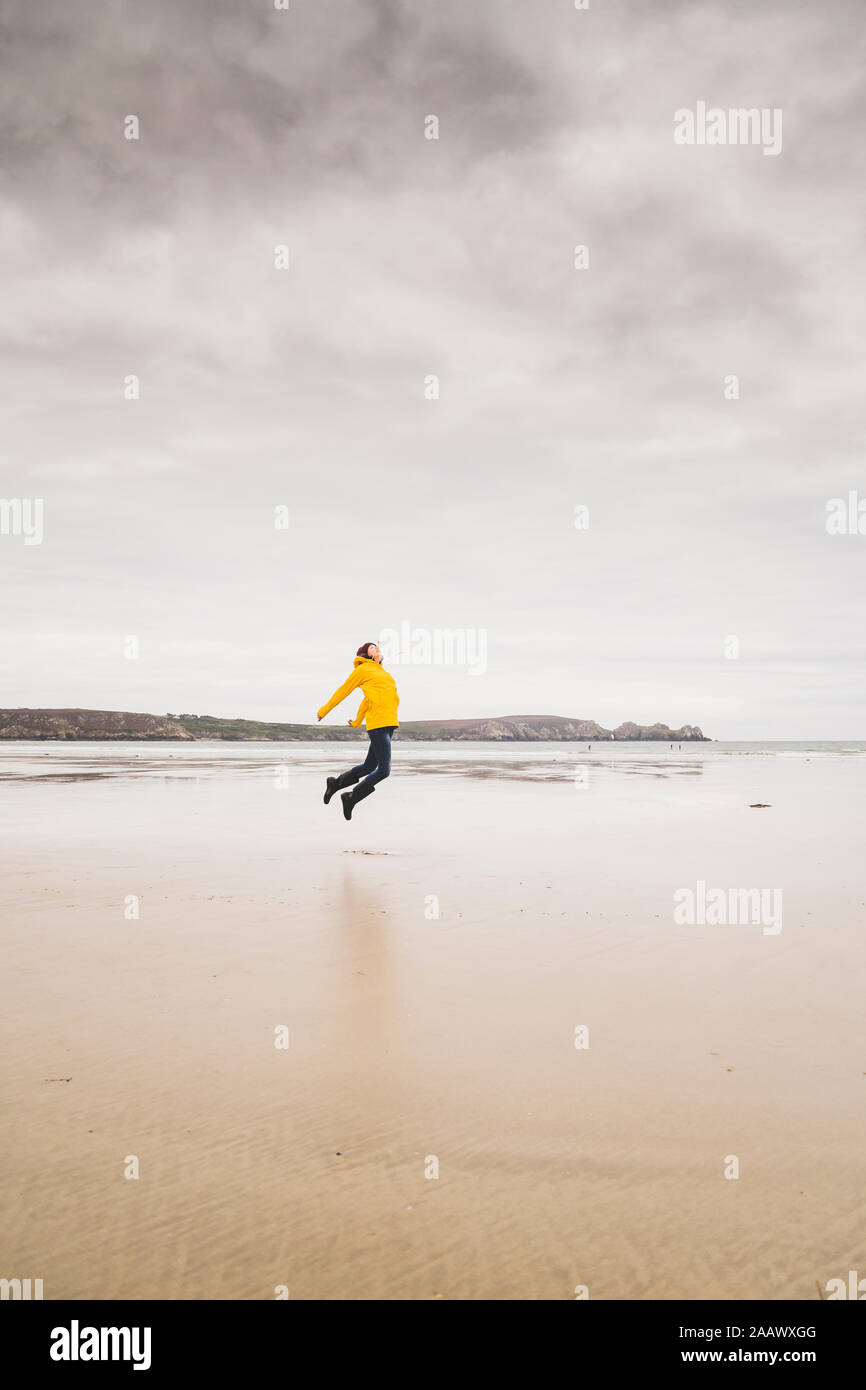 Jeune femme portant Veste pluie jaune sur la plage, Bretagne, France Banque D'Images