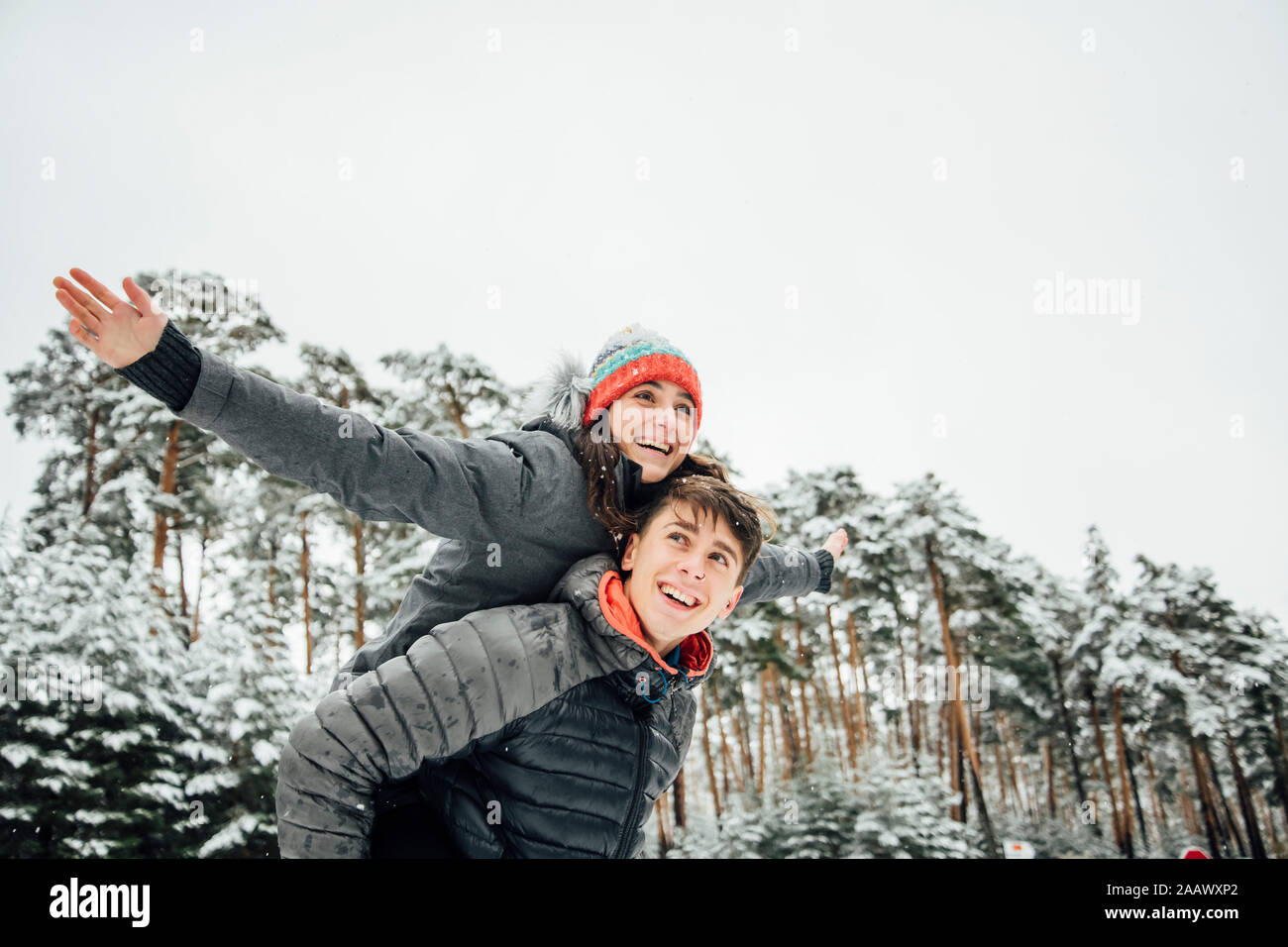 Portrait of smiling young man giving son heureux petite amie une piggyback ride en forêt d'hiver Banque D'Images