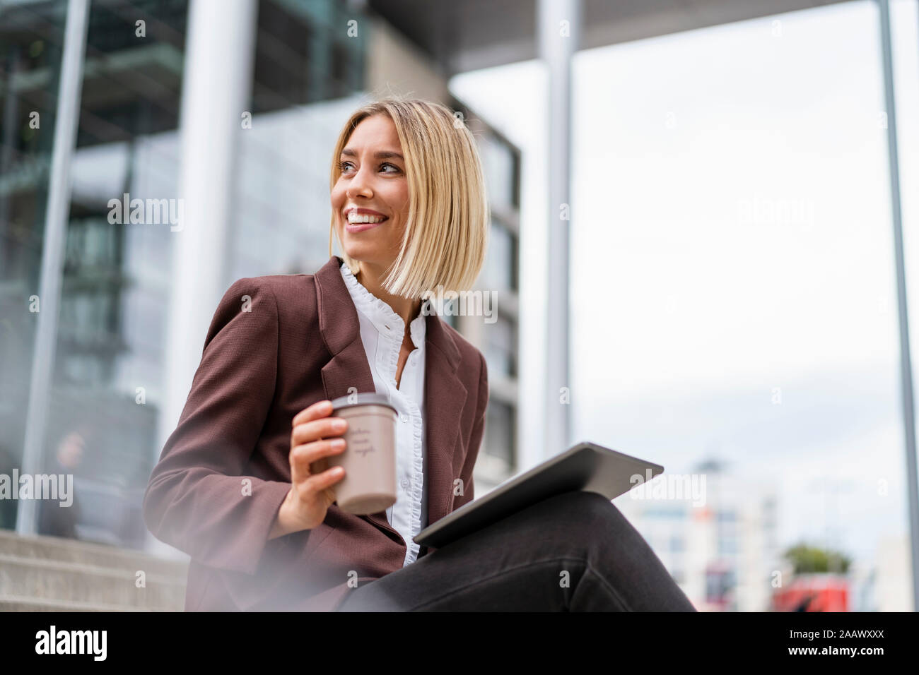 Smiling young businesswoman with tablet et café pour aller dans la ville Banque D'Images