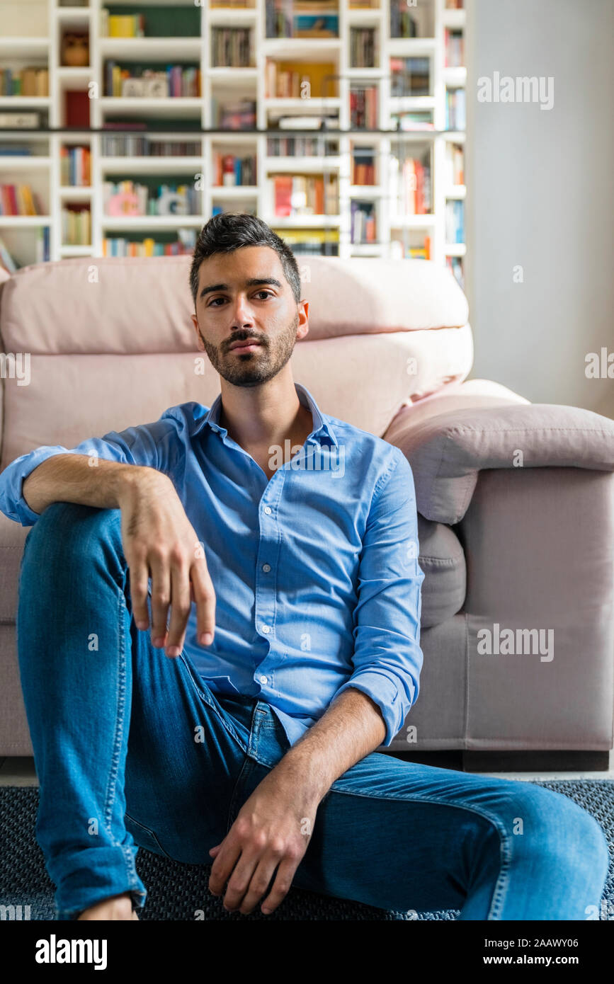 Portrait de jeune homme sérieux assis sur le plancher de salle de séjour à la maison Banque D'Images