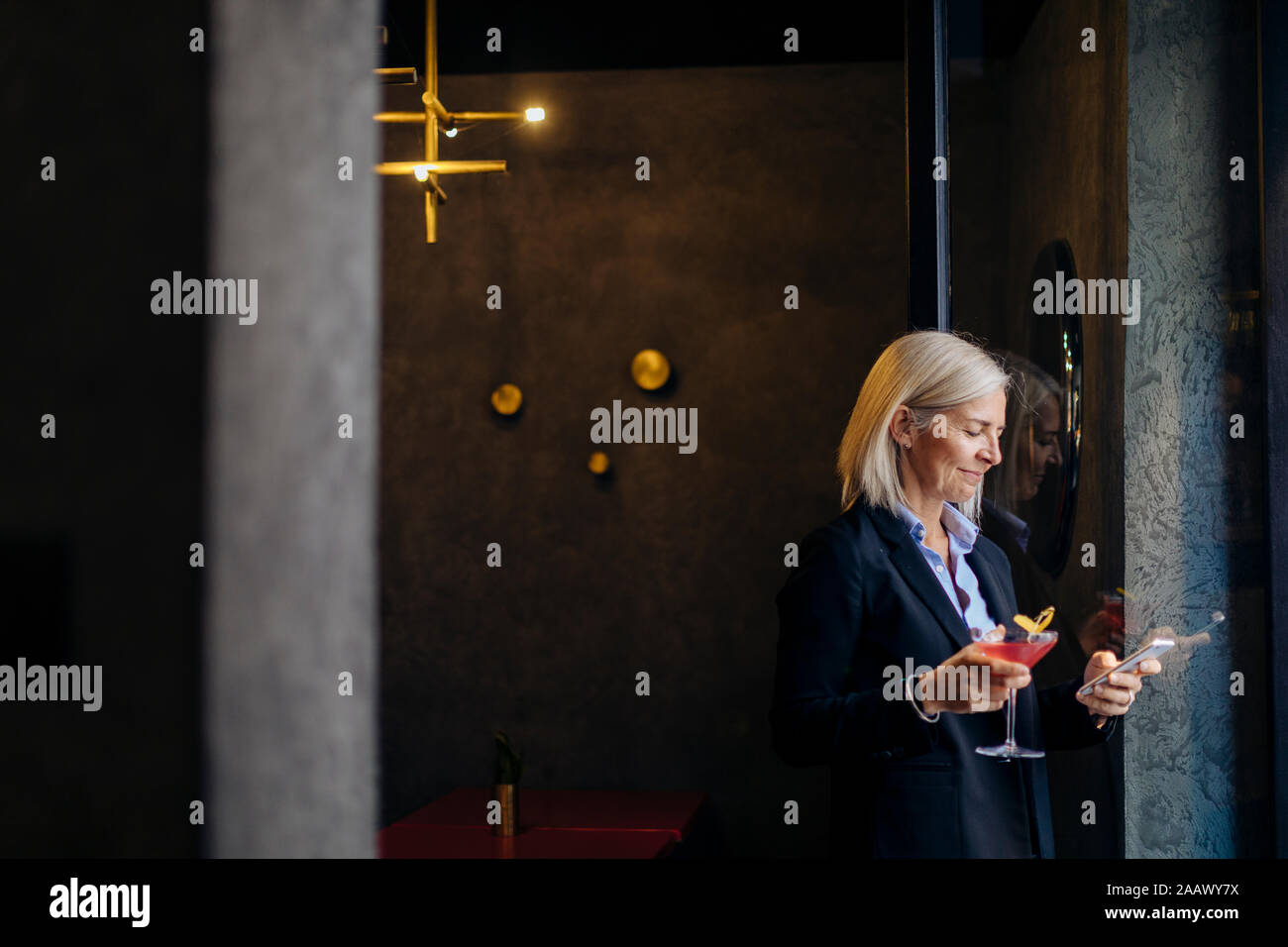 Femme d'âge mûr en prenant un cocktail après le travail, using smartphone Banque D'Images