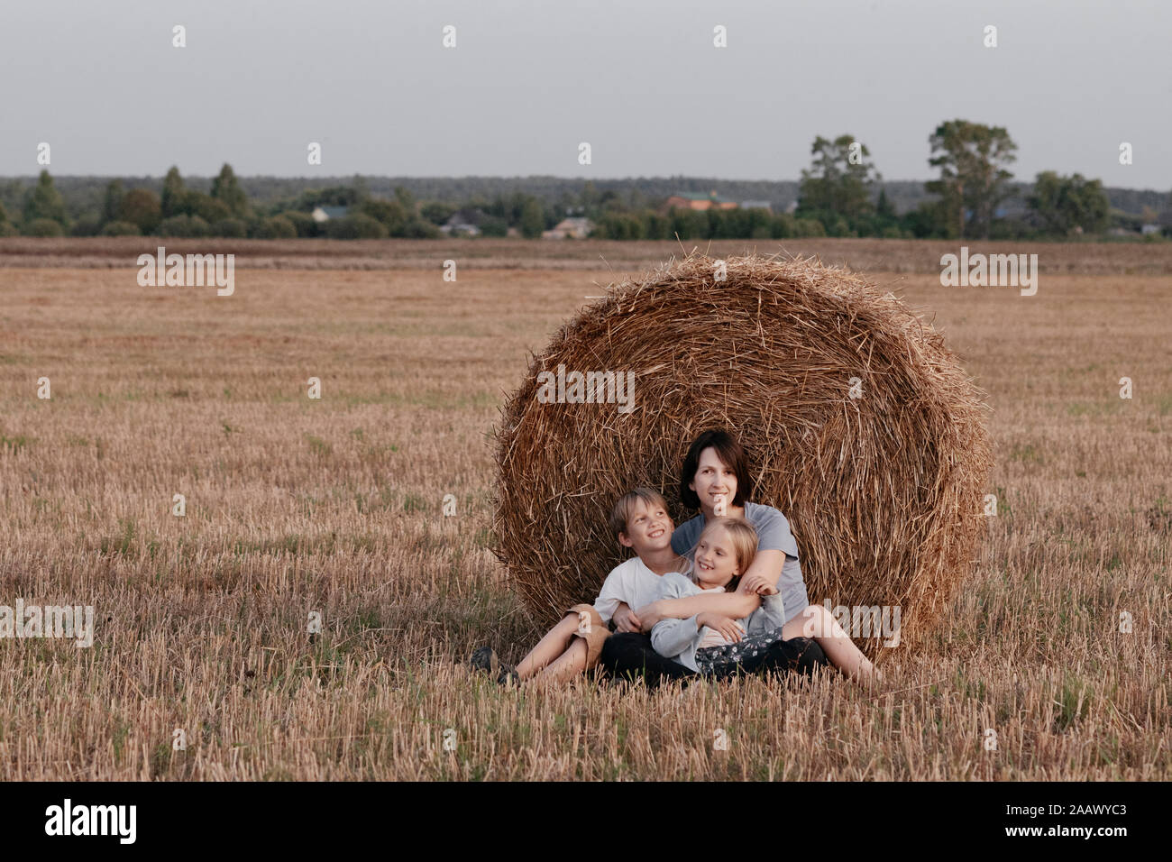 Femme avec deux enfants assis près d'une botte sur un champ de chaumes Banque D'Images
