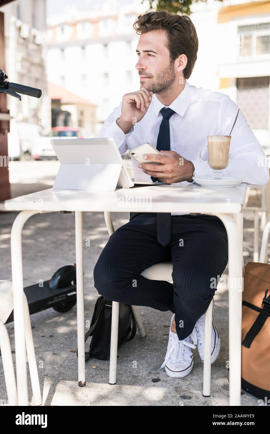 Young businessman using tablet and mobile phone dans un café dans la ville, Lisbonne, Portugal Banque D'Images