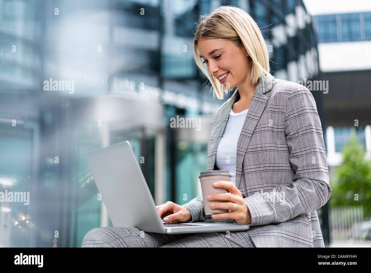 Smiling young businesswoman using laptop in the city Banque D'Images