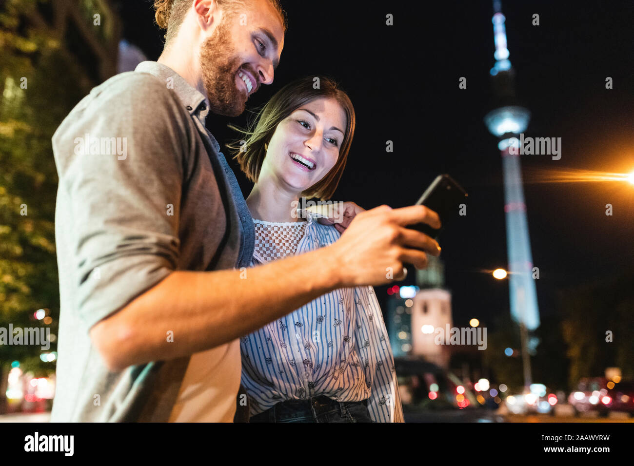 Couple heureux à l'aide de smartphones dans la ville la nuit, Fernsehturm en arrière-plan, Berlin, Allemagne Banque D'Images