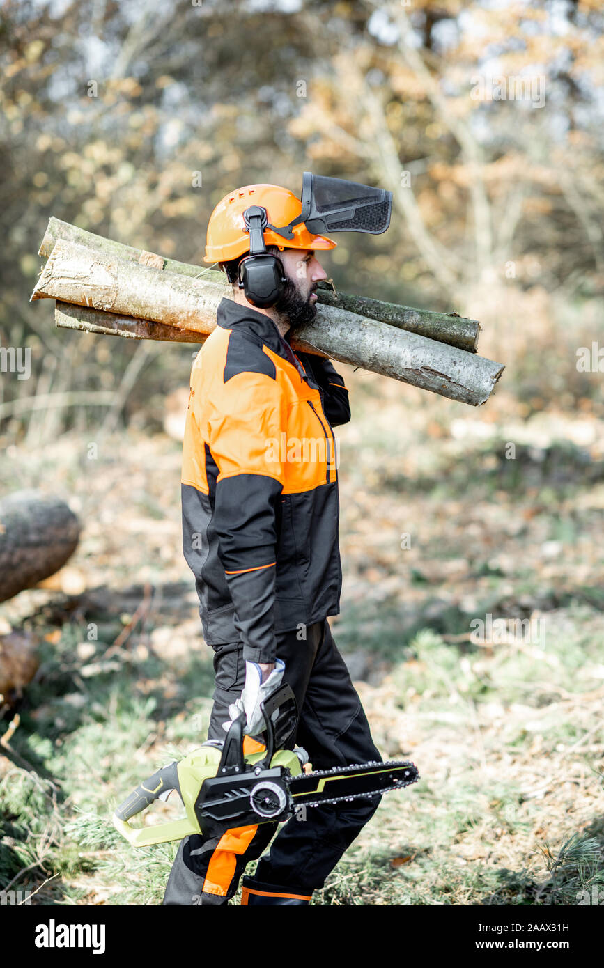 Vêtements de protection en bûcheron professionnel avec une tronçonneuse  transportant des troncs pendant le travail sur l'exploitation forestière  dans la forêt de pins Photo Stock - Alamy