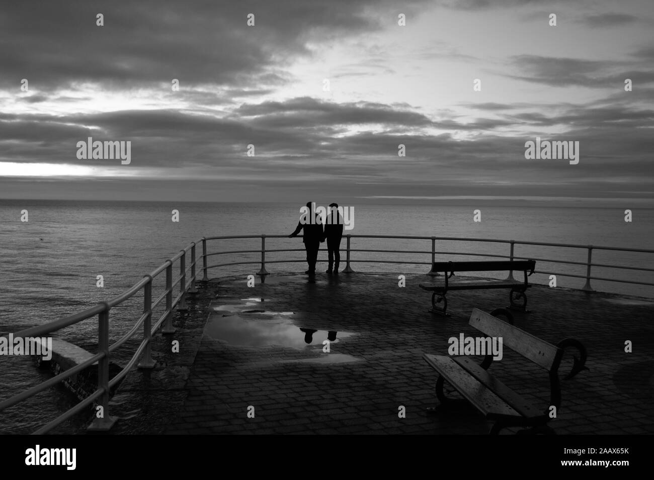 Le noir et blanc couple holding hands in silhouette debout regardant le coucher de soleil sur la mer à l'ouest du pays de Galles Aberystwyth UK Banque D'Images