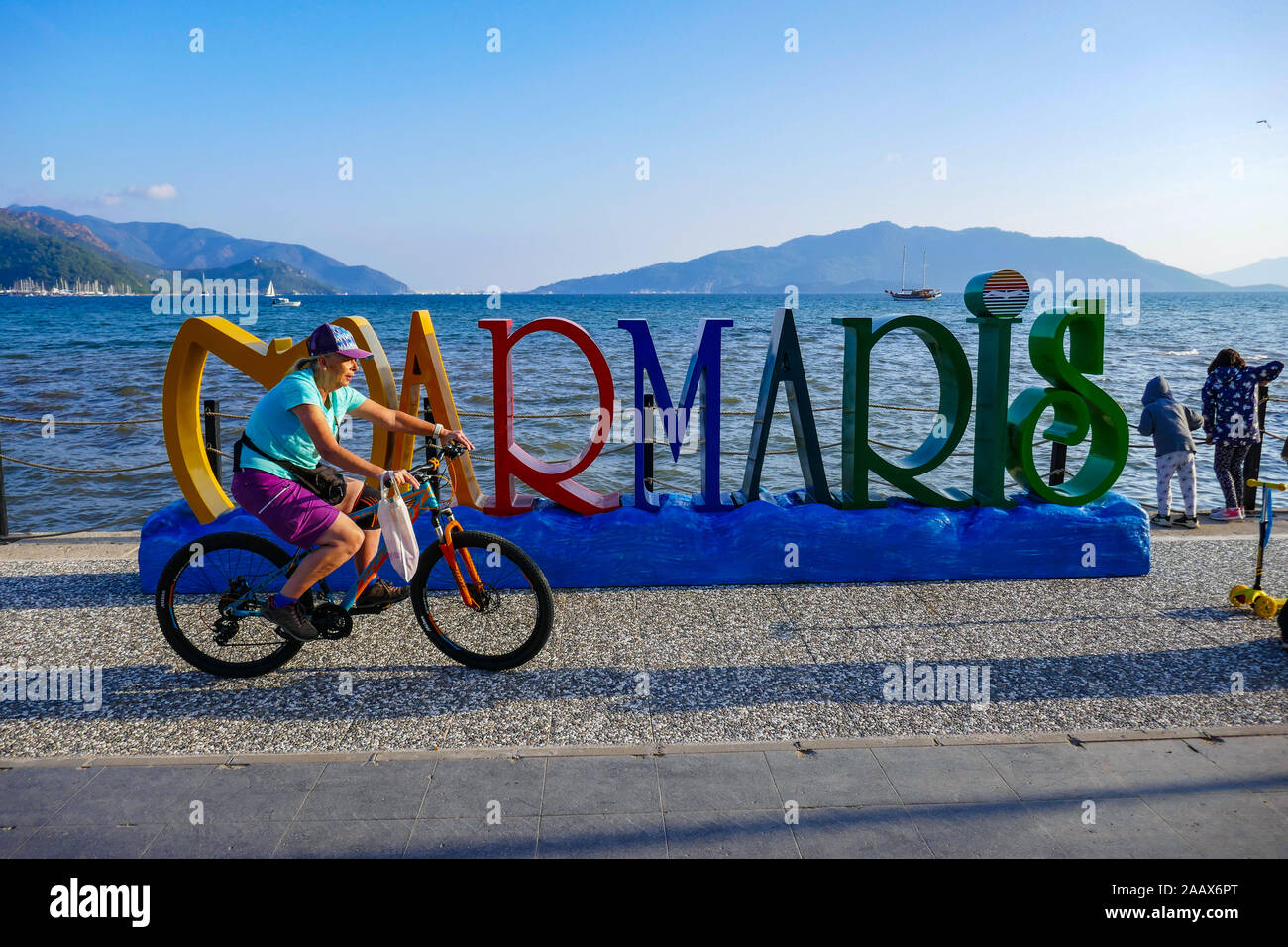 Femme à vélo sur front de mer, avec signe à Mamaris colorés, une ville balnéaire populaire dans le sud de la Turquie, le temps d'automne. Banque D'Images