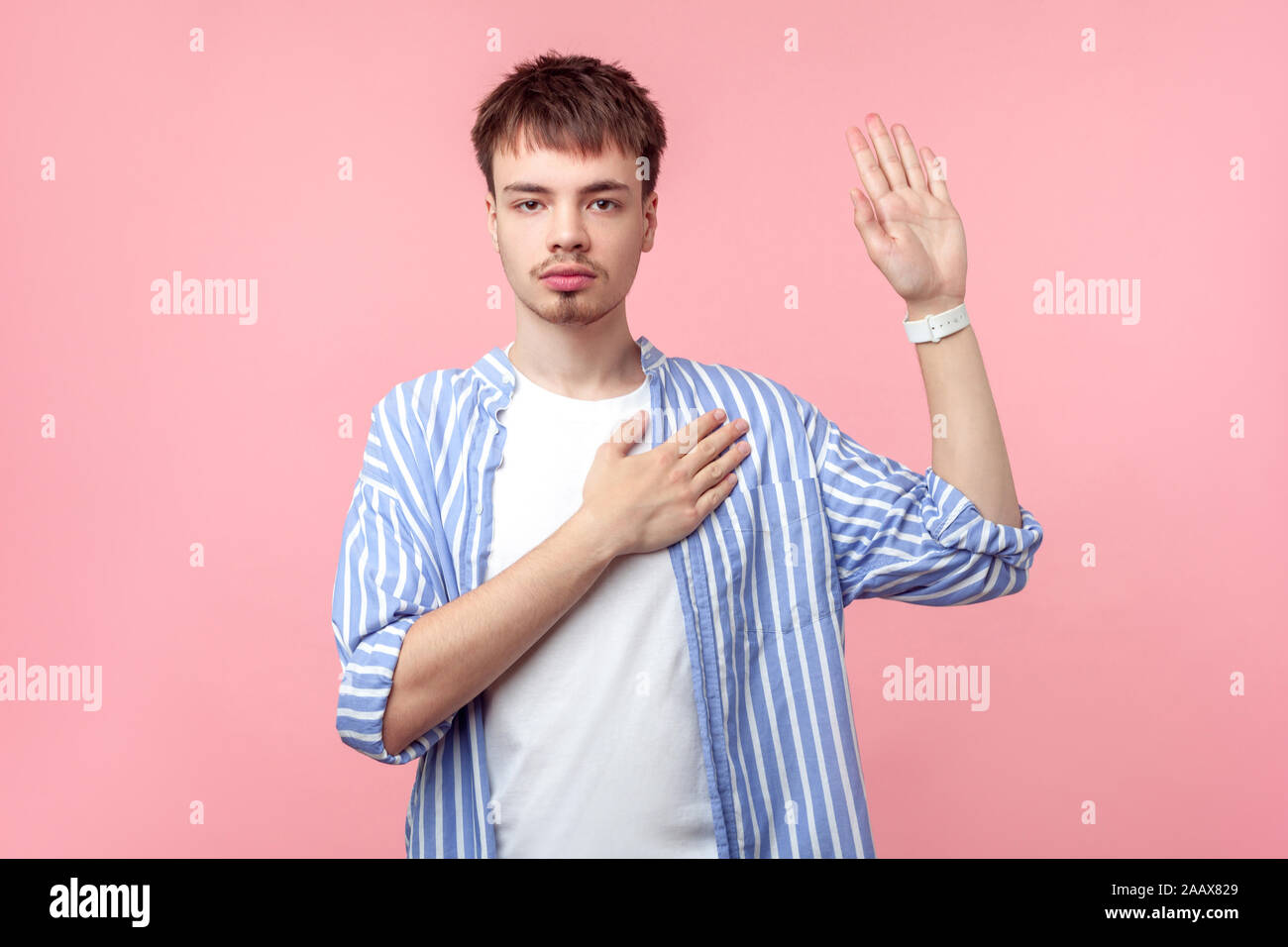 Je le jure ! Portrait de sérieux honnête homme aux cheveux brun avec petit barbe et moustache in casual chemise rayée en gardant la main sur la poitrine et faire de promesse d'ap Banque D'Images