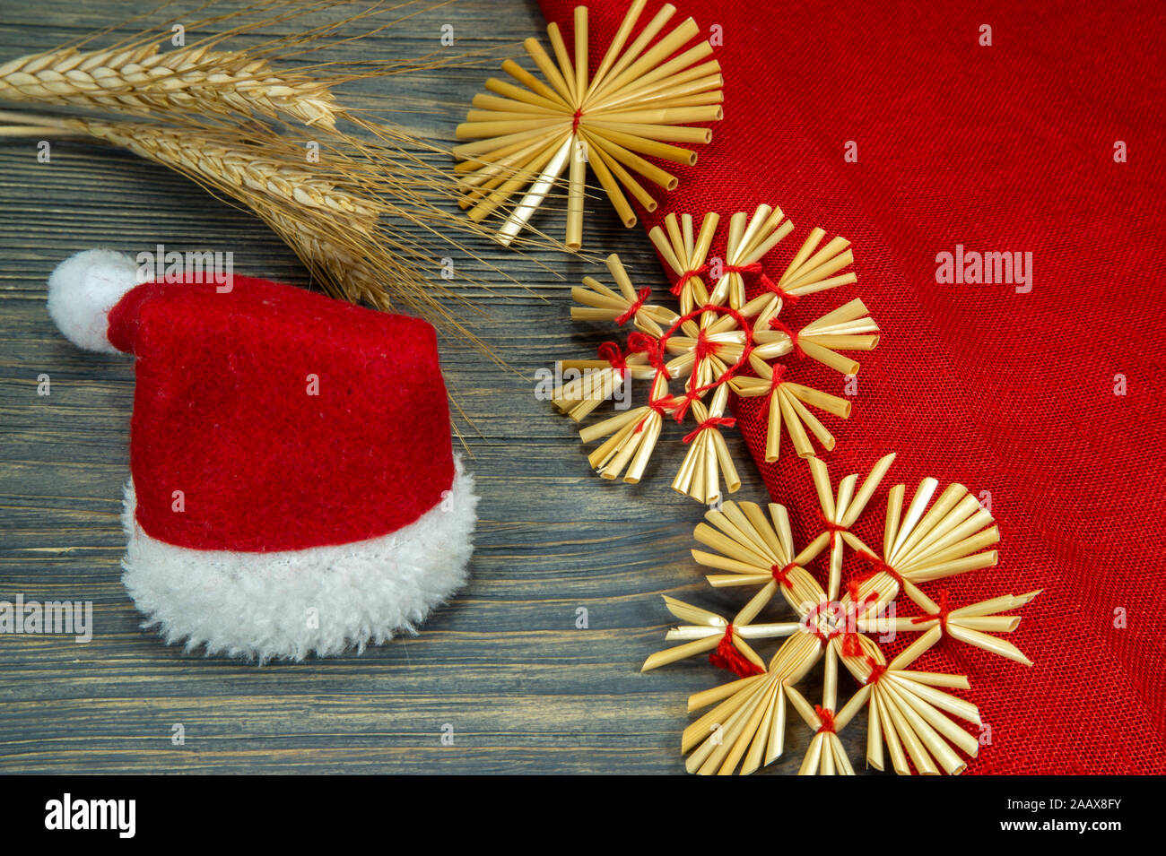 Noël encore la vie rustique avec des ornements de paille, une ambiance festive rouge Santa hat, tissu rouge correspondant et les oreilles de blé d'or sur une zone en bois Banque D'Images