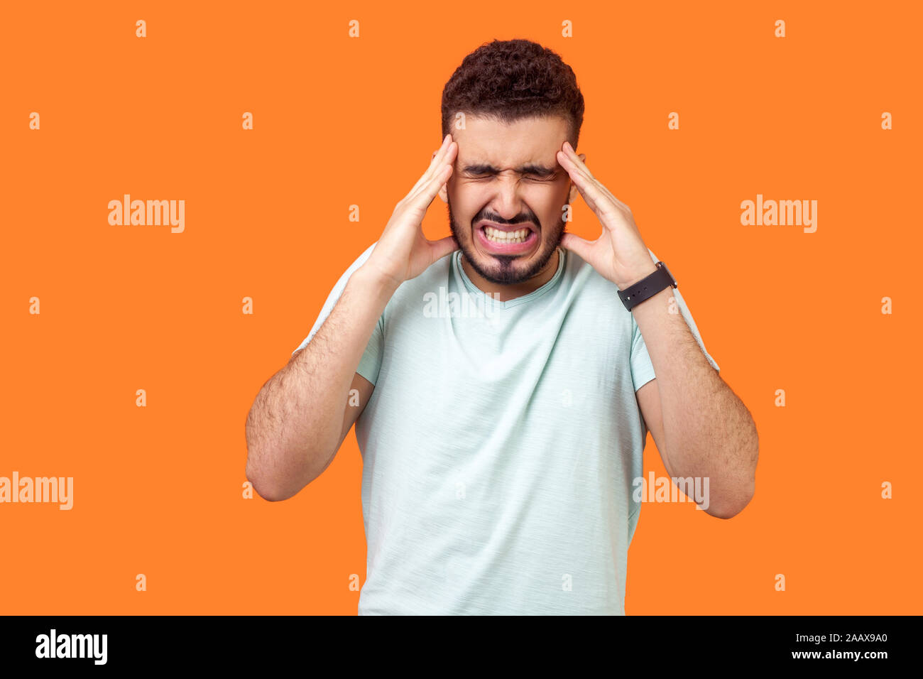 La douleur de tête. Portrait d'homme avec barbe brune malsaine in Casual t-shirt blanc touchant ses temples et souffrant de migraine, céphalée de tension intense Banque D'Images