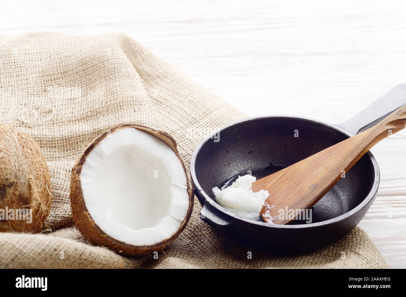 Coquille de noix de coco, avec de la viande, poêle en fonte et la spatule sur le chanvre sacs sur une table de cuisine en bois blanc Banque D'Images