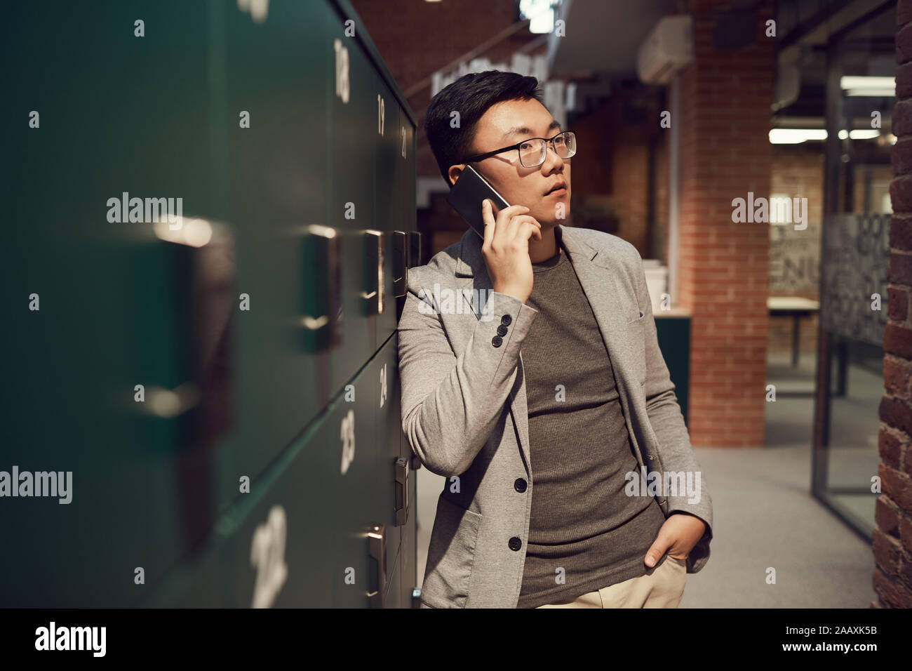 Jusqu'à la taille de l'Asian businessman portrait parlant par permanent smartphone par casiers dans un bureau moderne, copy space Banque D'Images