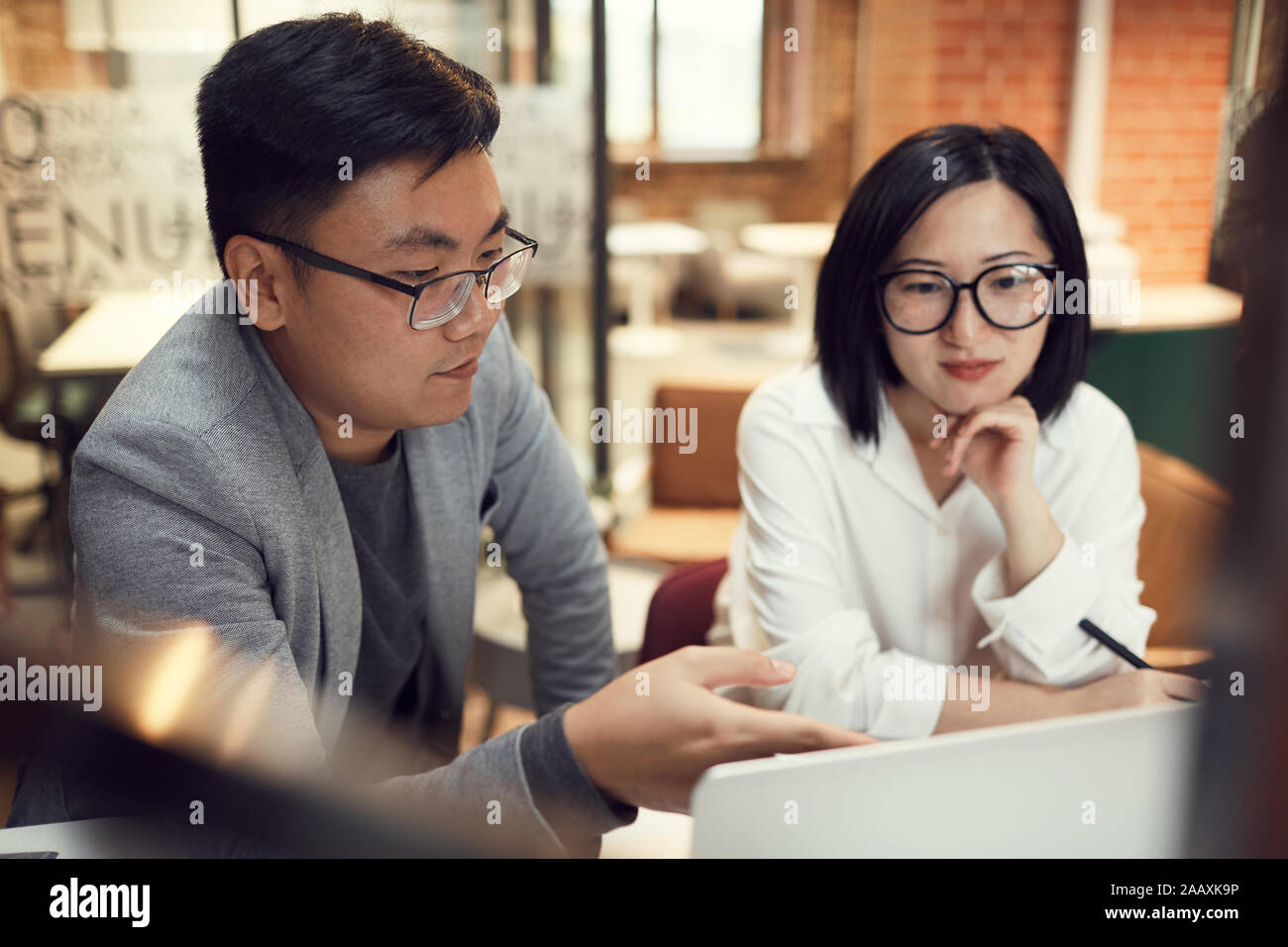 Portrait de deux affaires asiatiques modernes discuter projet de démarrage en pointant sur laptop in office Banque D'Images