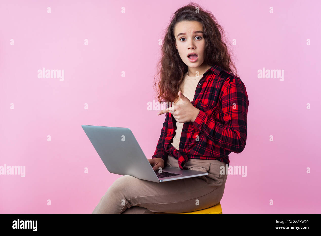 Portrait d'utilisateur d'ordinateur frustrés, teen girl with curly cheveux brune chemise à carreaux en pointant sur un ordinateur portable, l'air inquiet à propos de erreur de logiciel, prog Banque D'Images