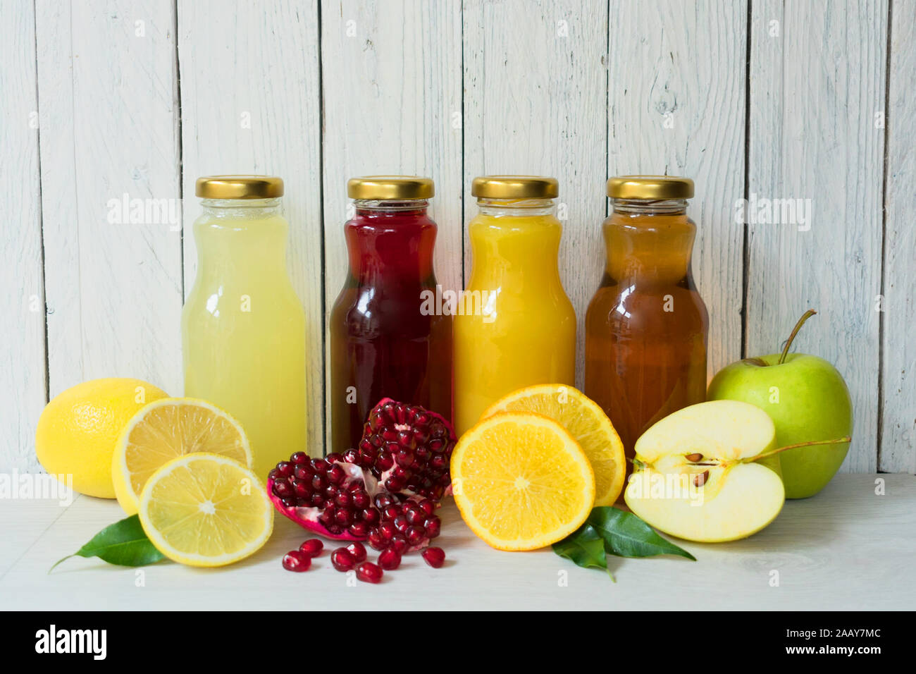 Quatre types de jus (grenade, pomme, citron, jus d'orange) dans des bouteilles en verre sur un fond de bois blanc Banque D'Images