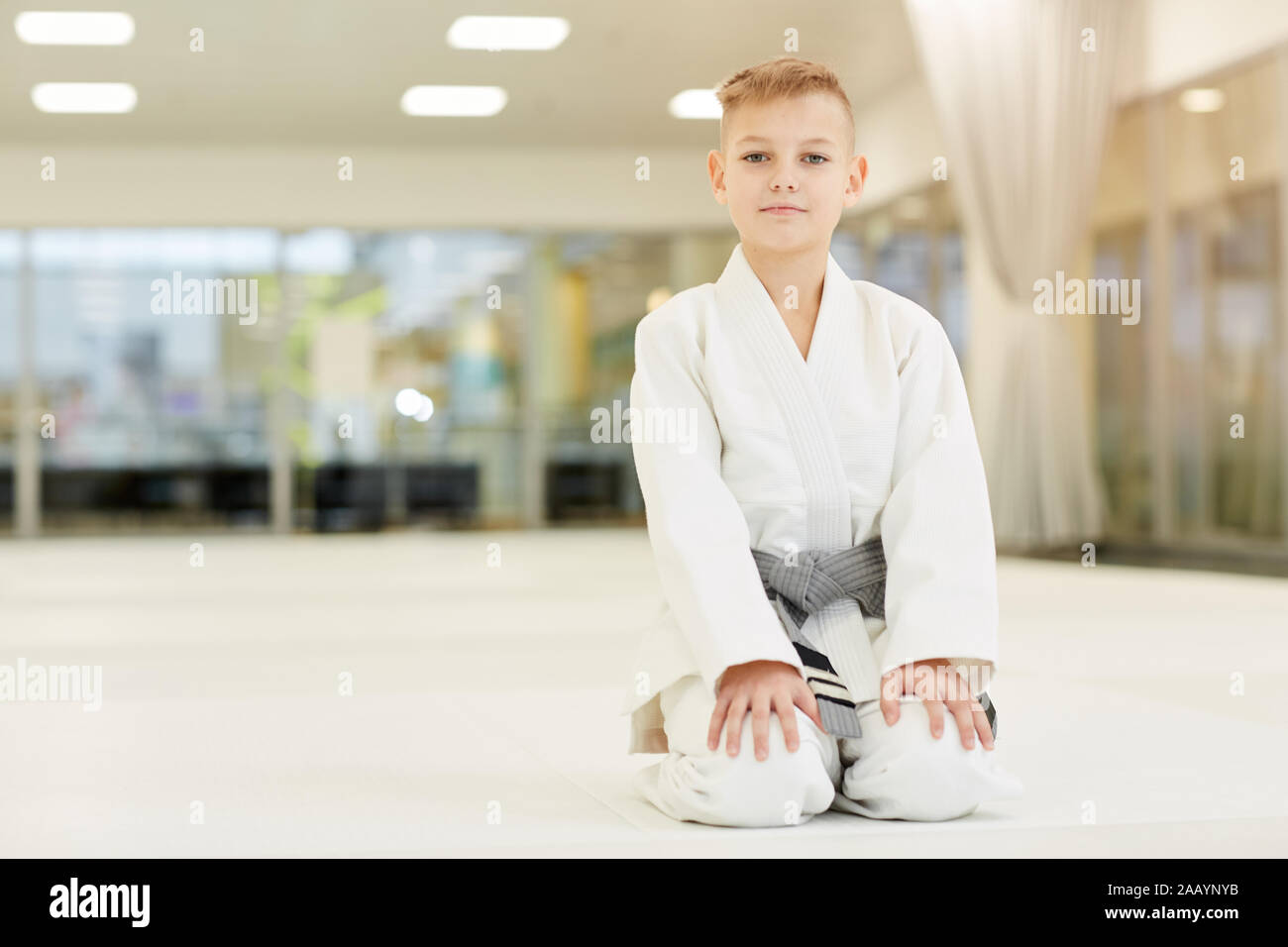 Portrait of little boy wearing kimono blanc assis sur le plancher et looking at camera il prêt pour l'entraînement sportif Banque D'Images