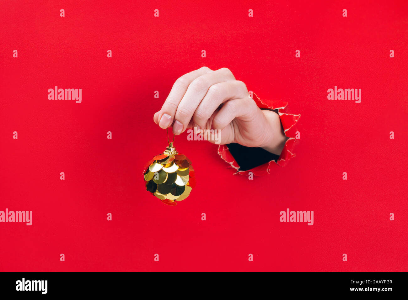 Femme hand holding Christmas bauble doré à travers un trou dans le fond rouge. Banque D'Images