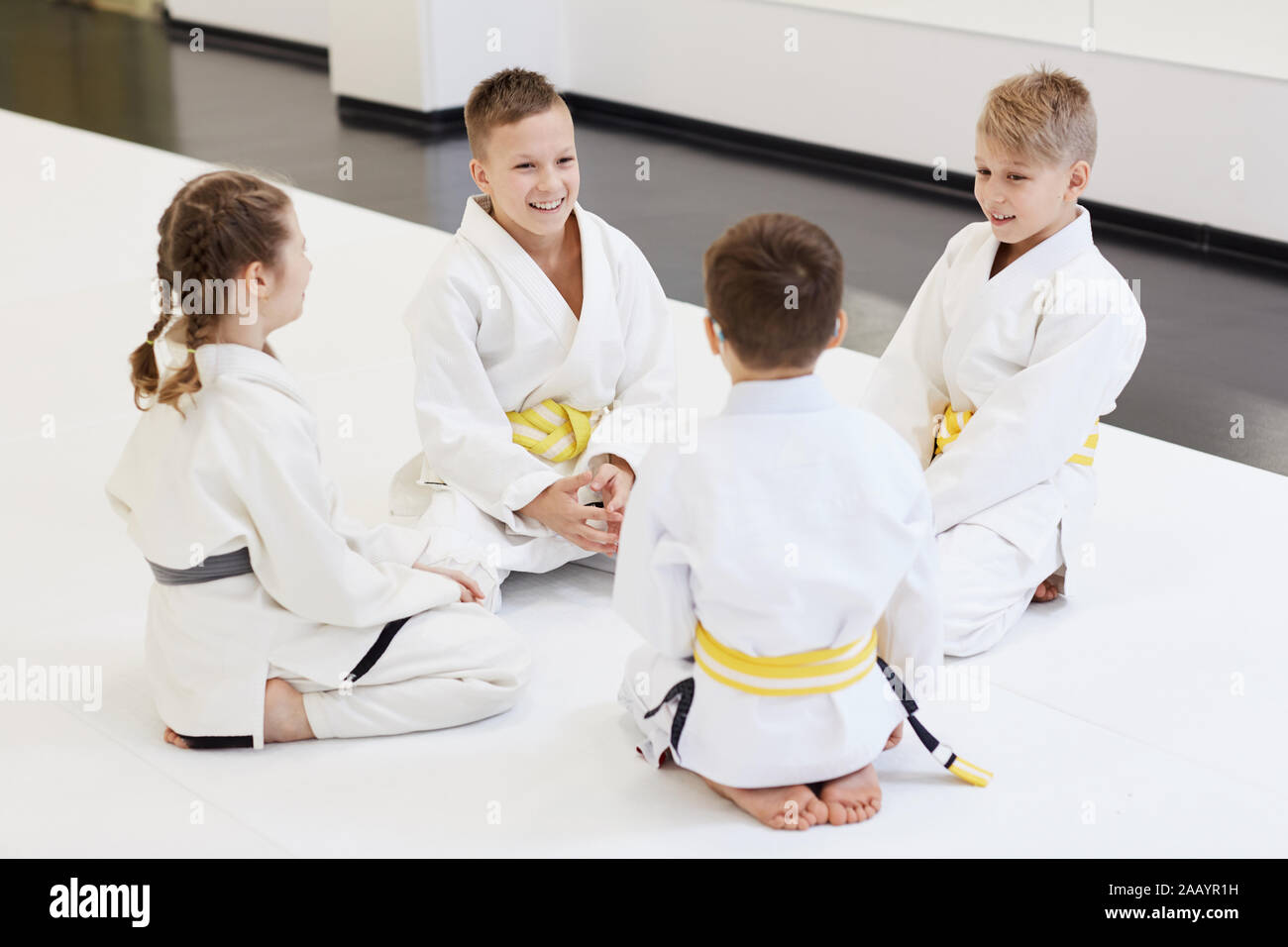 Groupe d'enfants assis sur le plancher ensemble et à se parler avant de l'entraînement sportif dans le karaté dans la salle de sport Banque D'Images