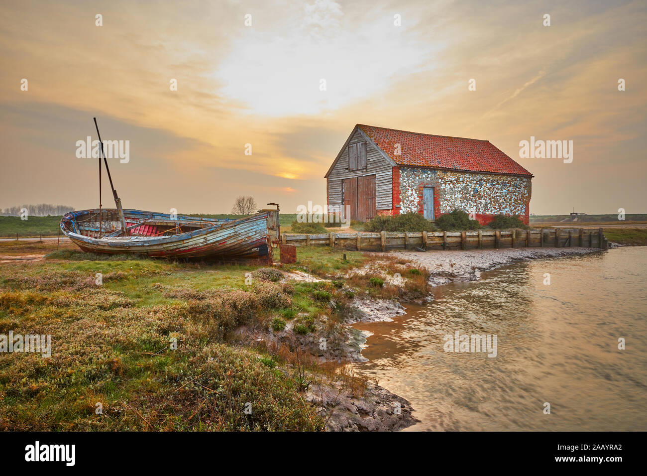Vieux bateau de pêche traditionnel en bois près de la vieille Grange à charbon à Thornham Old Harbour sur la côte nord de Norfolk rétroéclairé par le soleil de soirée T5XJ8T Banque D'Images