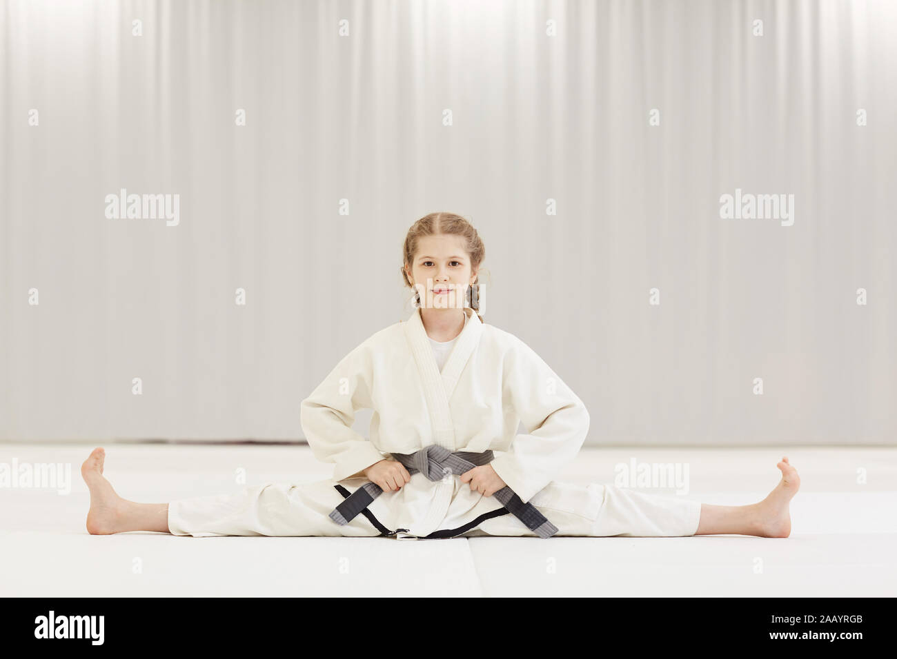 Portrait de petite fille en kimono blanc assis sur la ficelle et faire des exercices d'étirement pendant l'entraînement en karaté Banque D'Images