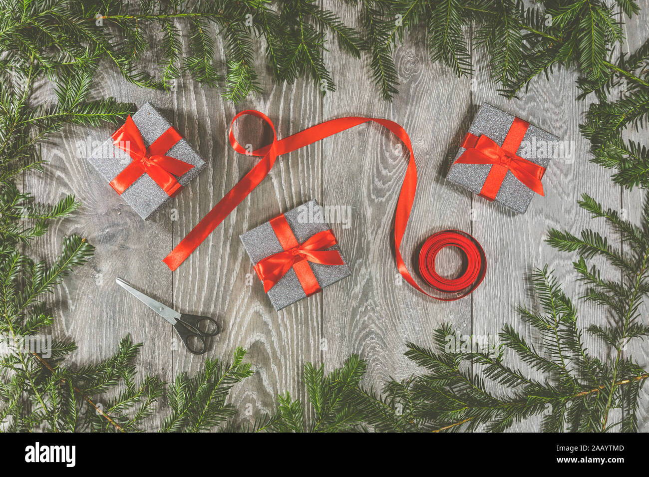 Trois cadeaux de Noël enveloppée par un ruban rouge, arc, également en photographie sont une paire de ciseaux et un rouleau de ruban et encadré par des branches d'arbre Banque D'Images