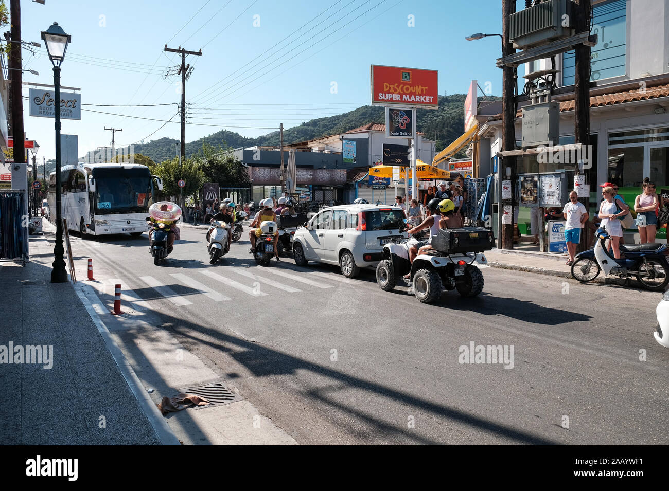 Une rue animée à Argassi sur l'île de Zakynthos avec un scooter de location conduit avec un donut gonflable au-dessus de la tête du conducteur. Banque D'Images