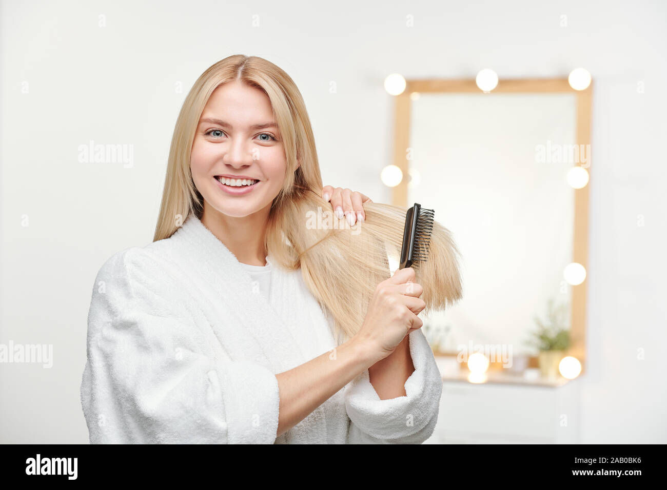 Heureux et en santé, jeune femme avec le sourire à pleines dents brosser ses longs cheveux blonds Banque D'Images