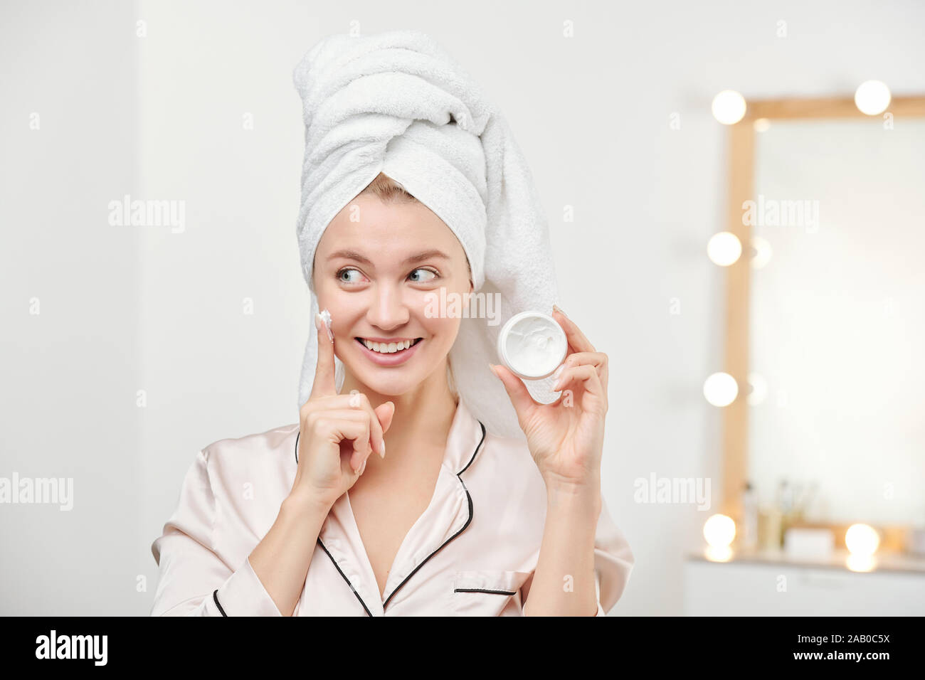 Fresh Young Beautiful woman with white towel on head appliqué sa crème visage Banque D'Images