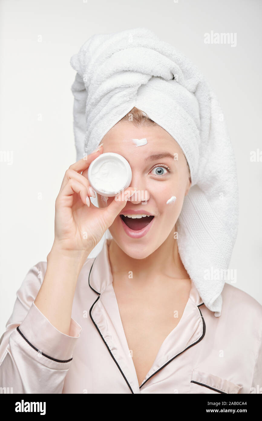 Jolie jeune femme extatique avec towel on head holding pot de crème visage Banque D'Images