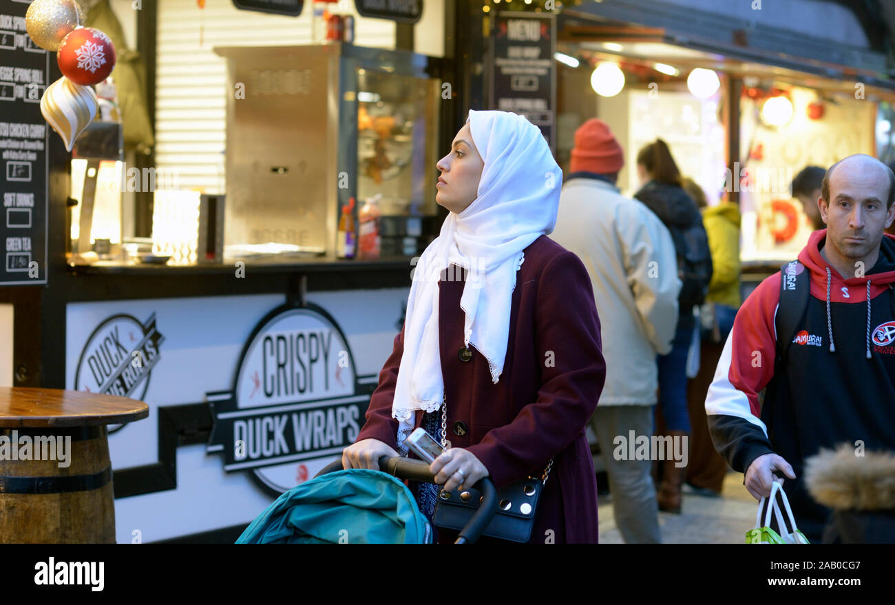 Femme musulmane en blanc hijab, à la recherche de stands de nourriture, féerie d'hiver. Banque D'Images