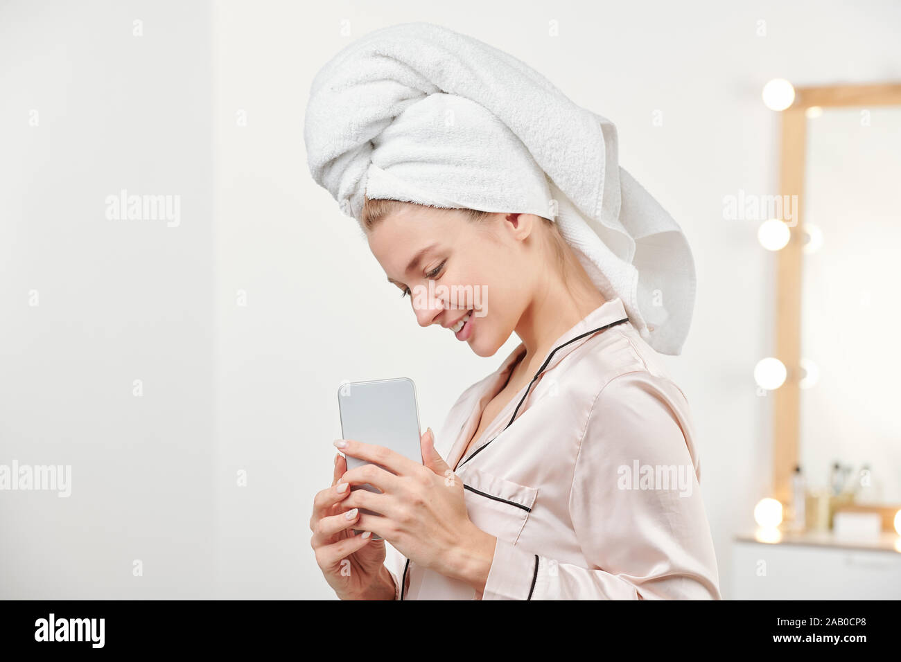 Pretty smiling girl with towel on head holding smartphone devant elle Banque D'Images