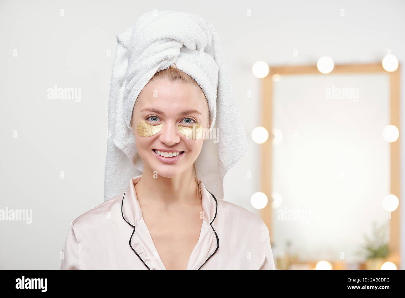Jolie jeune femme souriante avec une serviette sur la tête ayant sous-masque yeux Banque D'Images