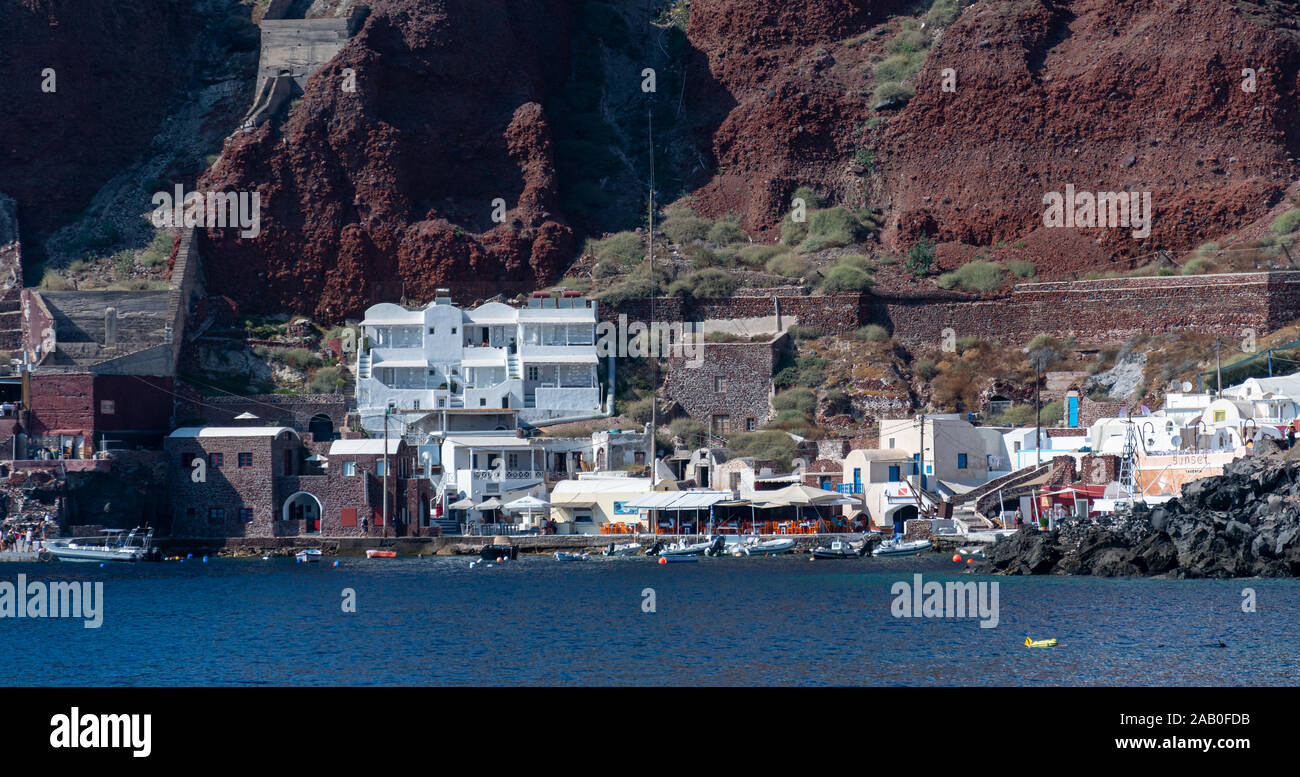 Oia, Grèce - 16 juillet 2019 : Des magasins, cafés et maisons du côté d'Oia dock comme vu de la mer Égée Banque D'Images