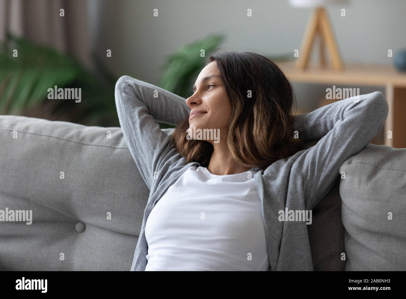 Femme mis les mains derrière la tête se pencha sur le divan se reposant à l'intérieur Banque D'Images