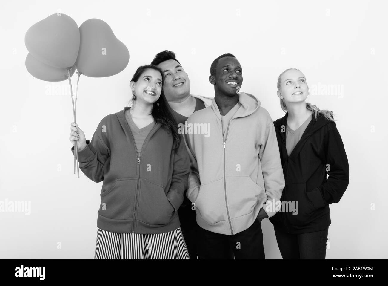 Studio shot of happy groupe diversifié de multi ethnic friends smiling et penser ensemble tout en maintenant bouquet de ballons en forme de coeur rouge Banque D'Images