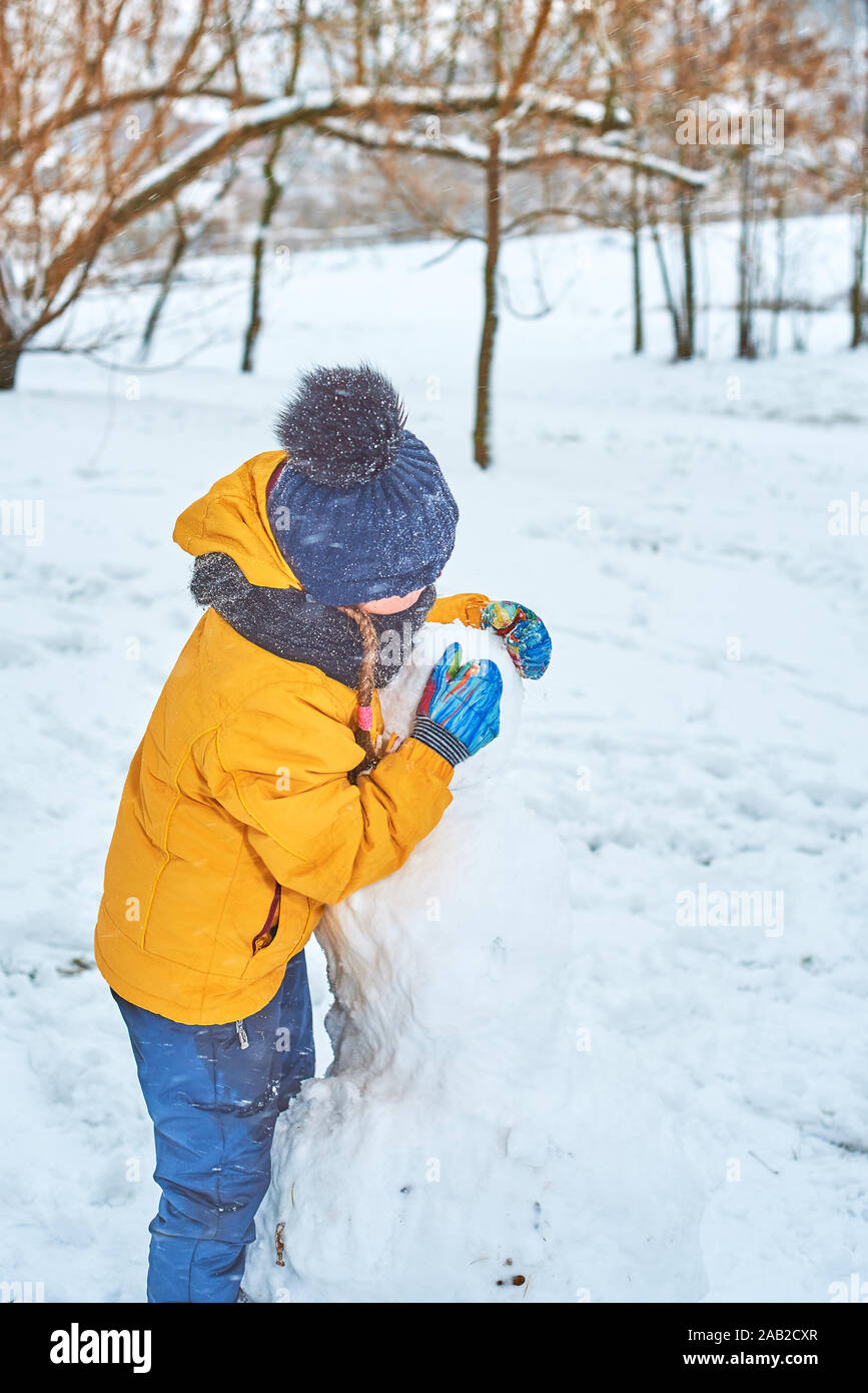 Petite fille sculpte un bonhomme de neige en hiver Banque D'Images