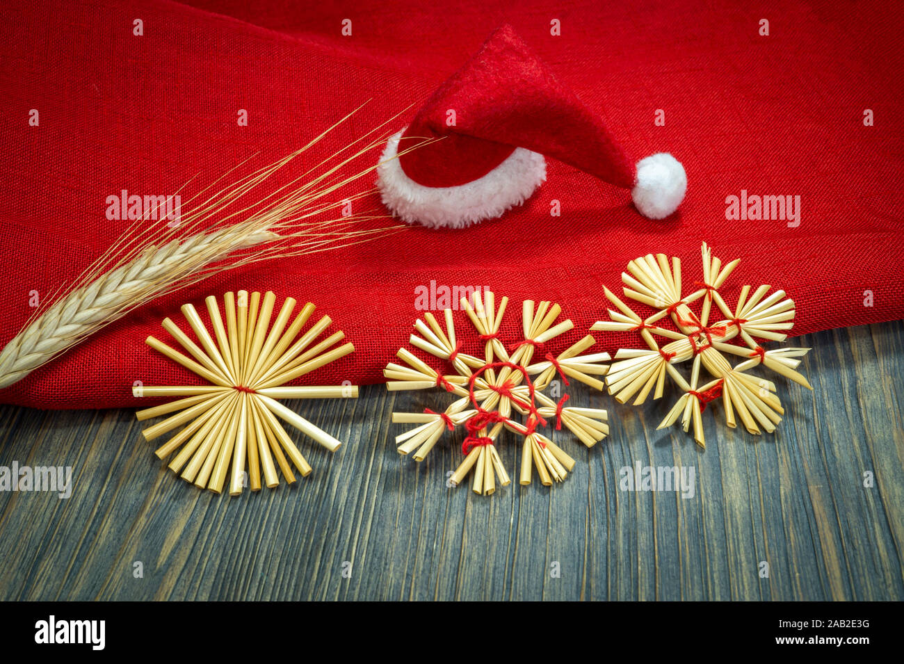 Noël encore la vie rustique avec des ornements de paille, une ambiance festive rouge Santa hat, tissu rouge correspondant et les oreilles de blé d'or sur une zone en bois Banque D'Images