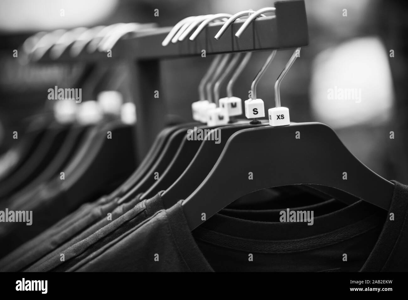 Une image noir et blanc de cintres suspendus dans le magasin, sur laquelle accrocher de simples t-shirts de différentes tailles. Banque D'Images
