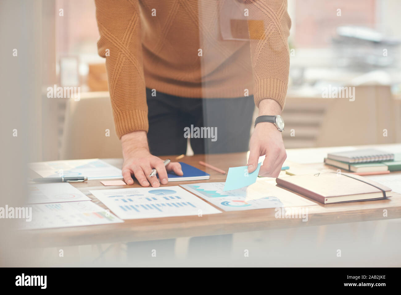 Cropped portrait of young businessman classement des documents et des données lors de la planification de projet derrière le verre wall in office, copy space Banque D'Images
