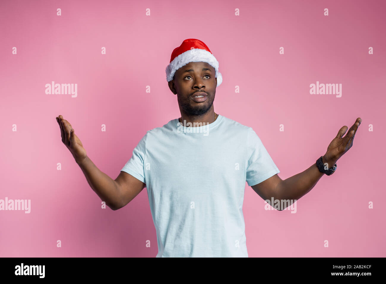 Jusqu'à la taille de balle déçu african american man étend les mains avec de l'indignation, wearing Santa hat, t shirt, jusqu'à la perplexité, isolé sur Rose Banque D'Images