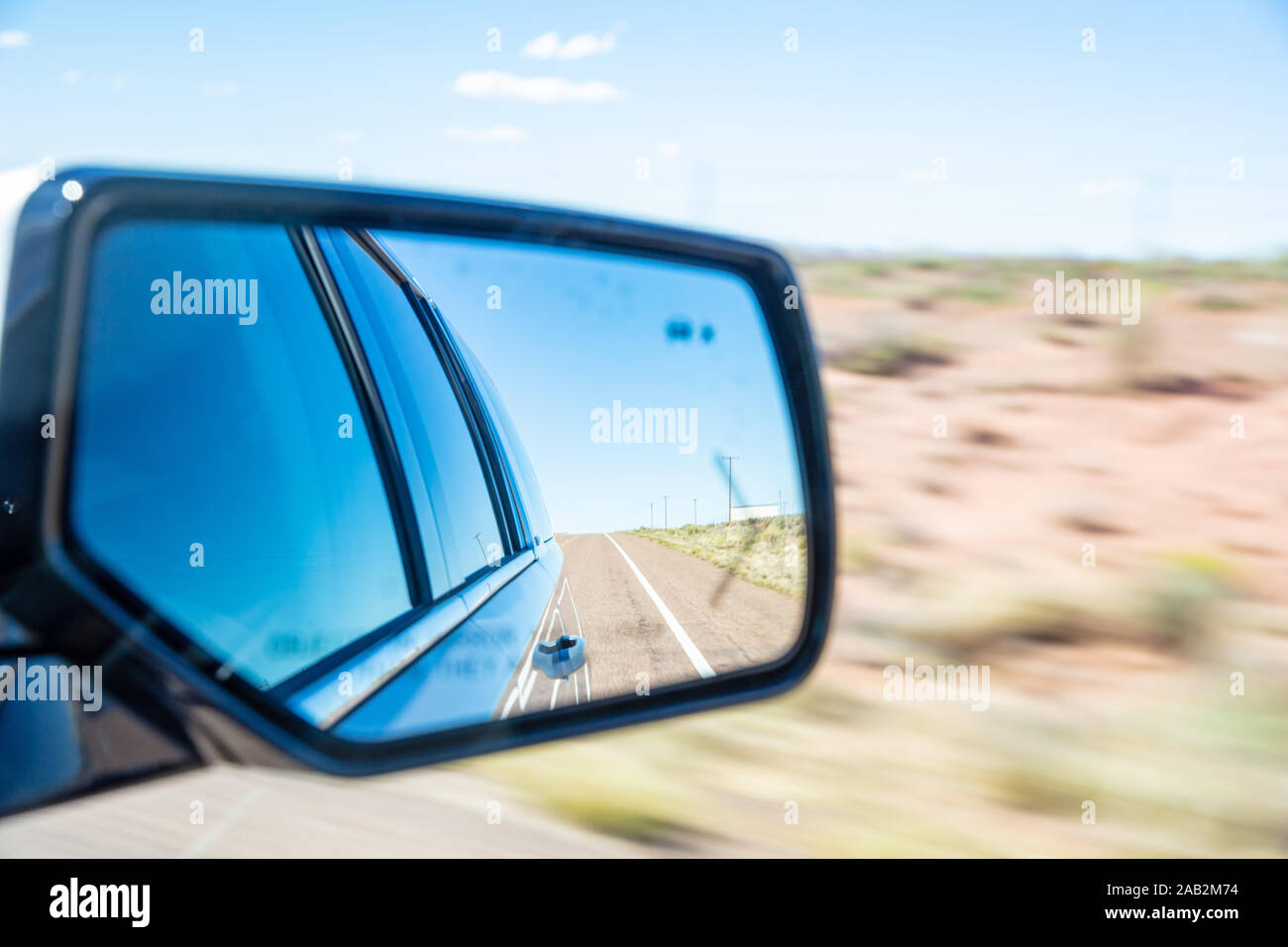 La conduite sur une route dans le désert américain. Freeway reflète dans une voiture wing mirror dans une journée de printemps, flou, fond du désert Banque D'Images