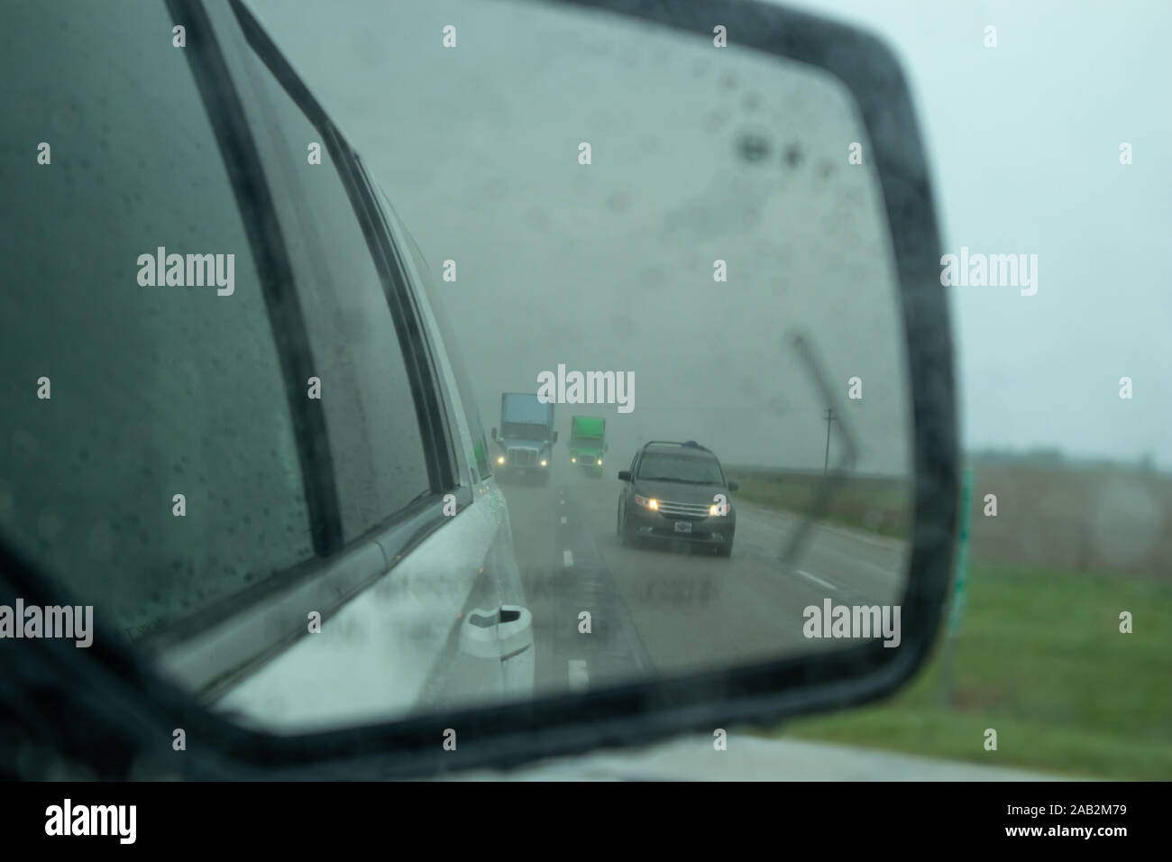 Conduire sur une route un jour de printemps pluvieux. Les véhicules circulant sur une autoroute aux États-Unis countrside reflète dans une voiture wing mirror lors d'une pluie, ciel nuageux Banque D'Images