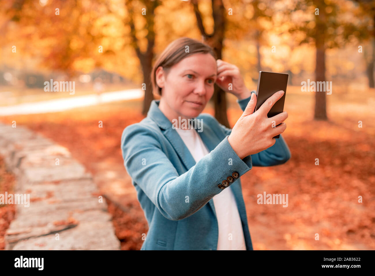 Smartphone avec selfies South et réglage de ses cheveux en automne parc, selective focus on mobile phone Banque D'Images