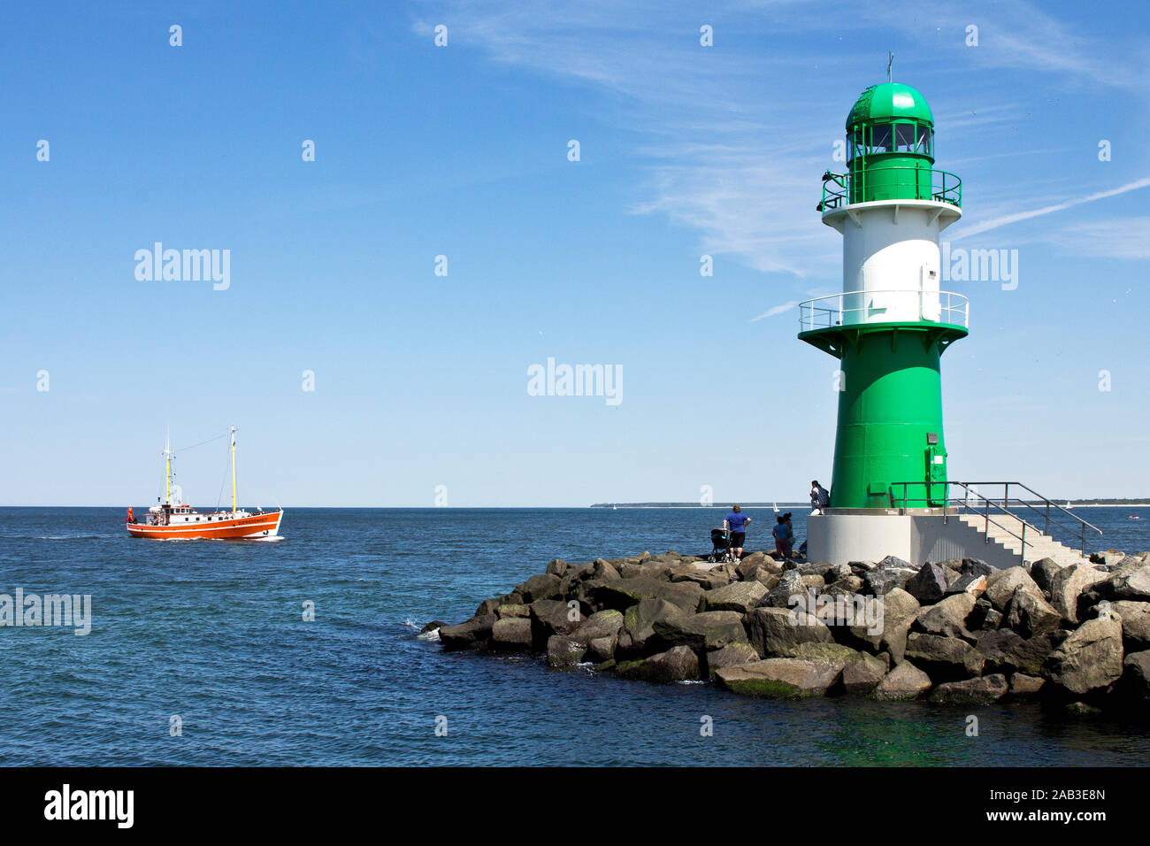 Ein Kutter läuft in den Hafen von Warnemünde ein, davor der grün-weiße Leuchtturm auf der Mole |Un cutter est dans le port de Warnemünde, en face de la Banque D'Images